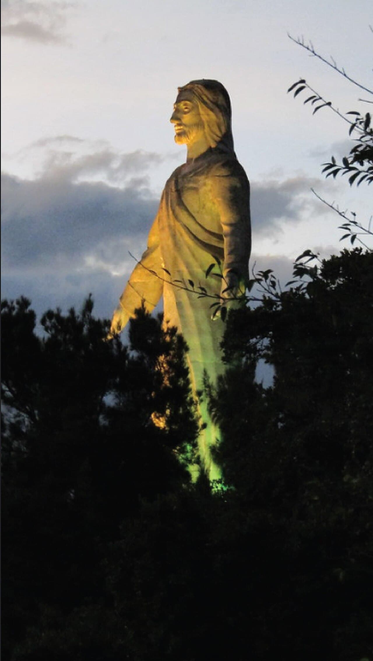 La estatua del Cristo del Picacho vista entre los árboles, iluminada al atardecer